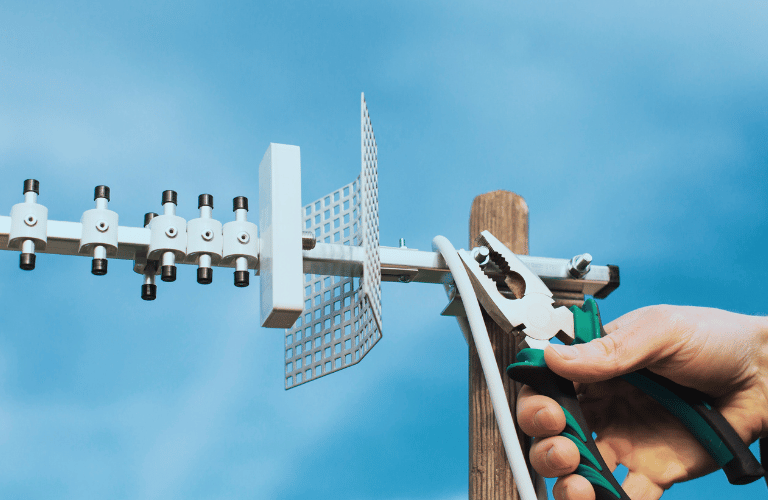 A technician's hand holds pliers to a pole for TV aerial installation.